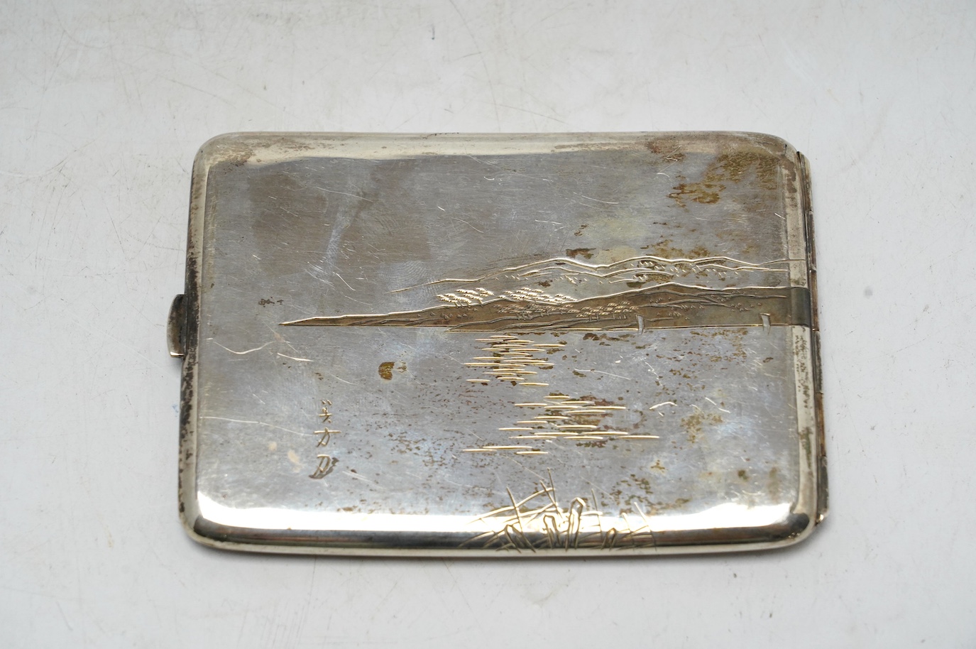 A white metal (stamped) and dark patinated Japanese silver cigarette case, decorated with a view of Mount Fuji, signed, 11cm, gross weight 113 grams. Condition - fair